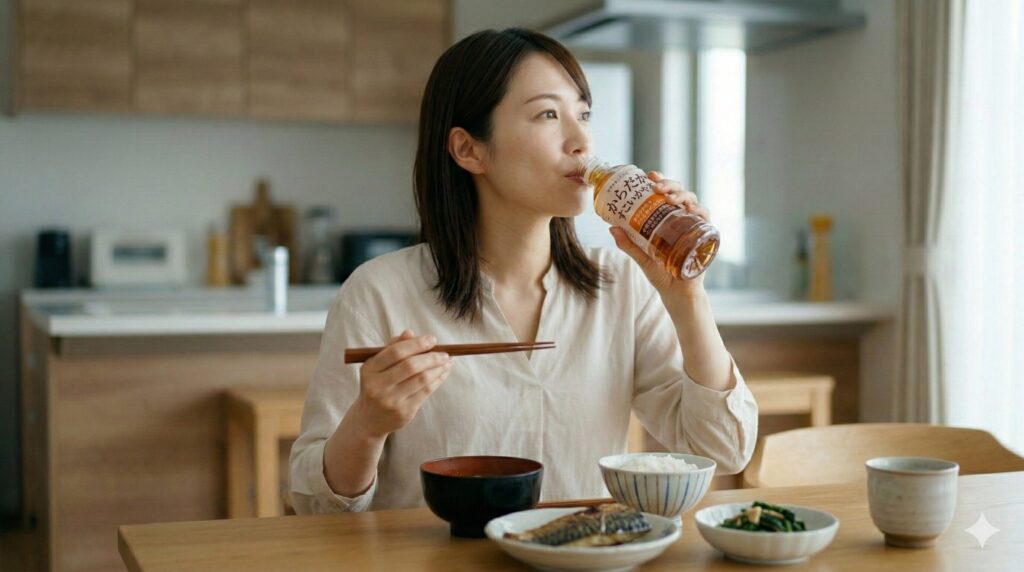 焼き魚や惣菜などの和食ランチを食べながら、からだすこやか茶W+を飲む日本人女性。日本の家庭のキッチン。